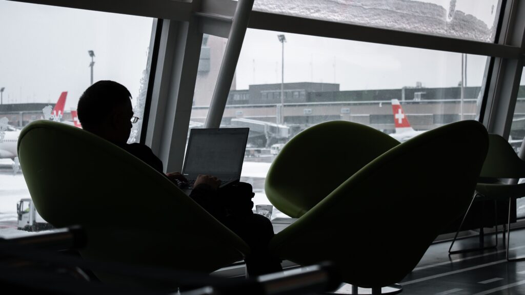 Traveler using a laptop at an airport while planning flights and managing airline loyalty status.