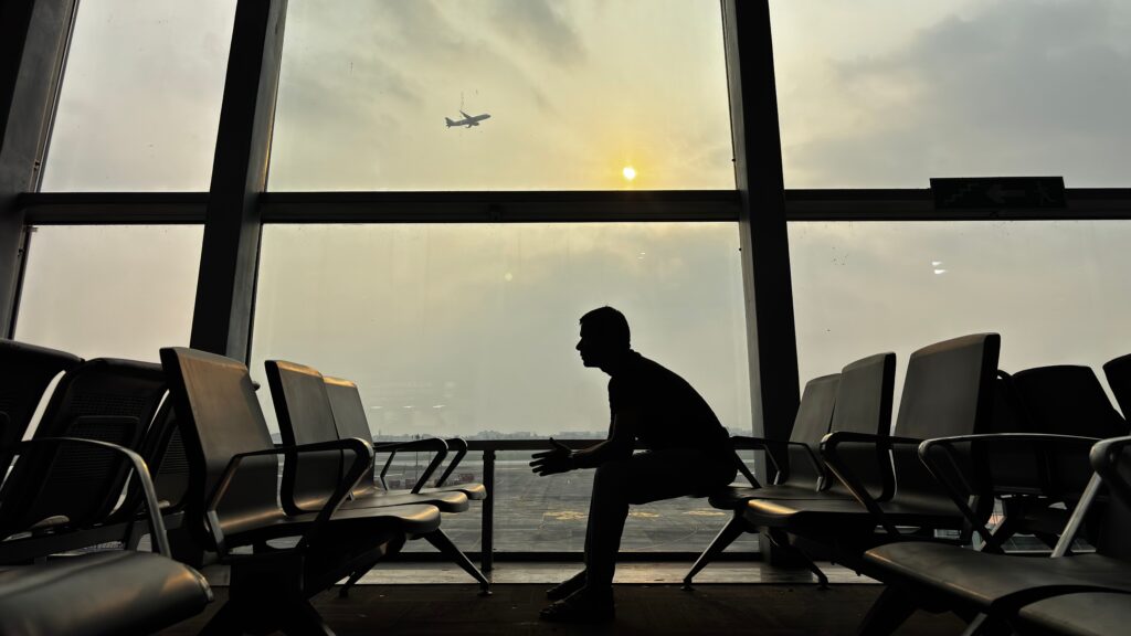 Silhouette of a traveler sitting alone in an airport terminal watching a plane at sunset, representing the pursuit of airline elite status and frequent flying.